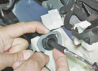 Отожмите пальцем пластмассовый фиксатор наконечника оболочки троса управления коробкой передач на автомобиле Hyundai Solaris